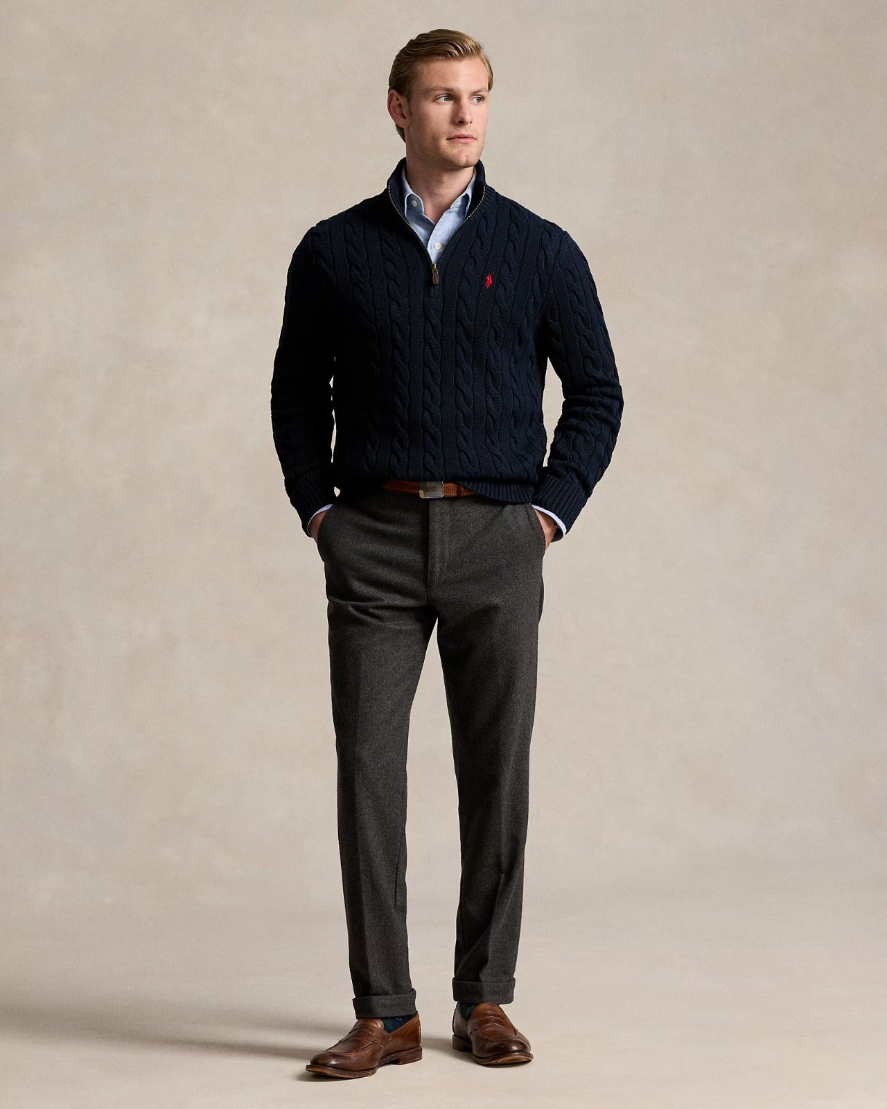 Model wearing a cable-knit quarter-zip sweater with a mockneck, paired with smart trousers and brown shoes.