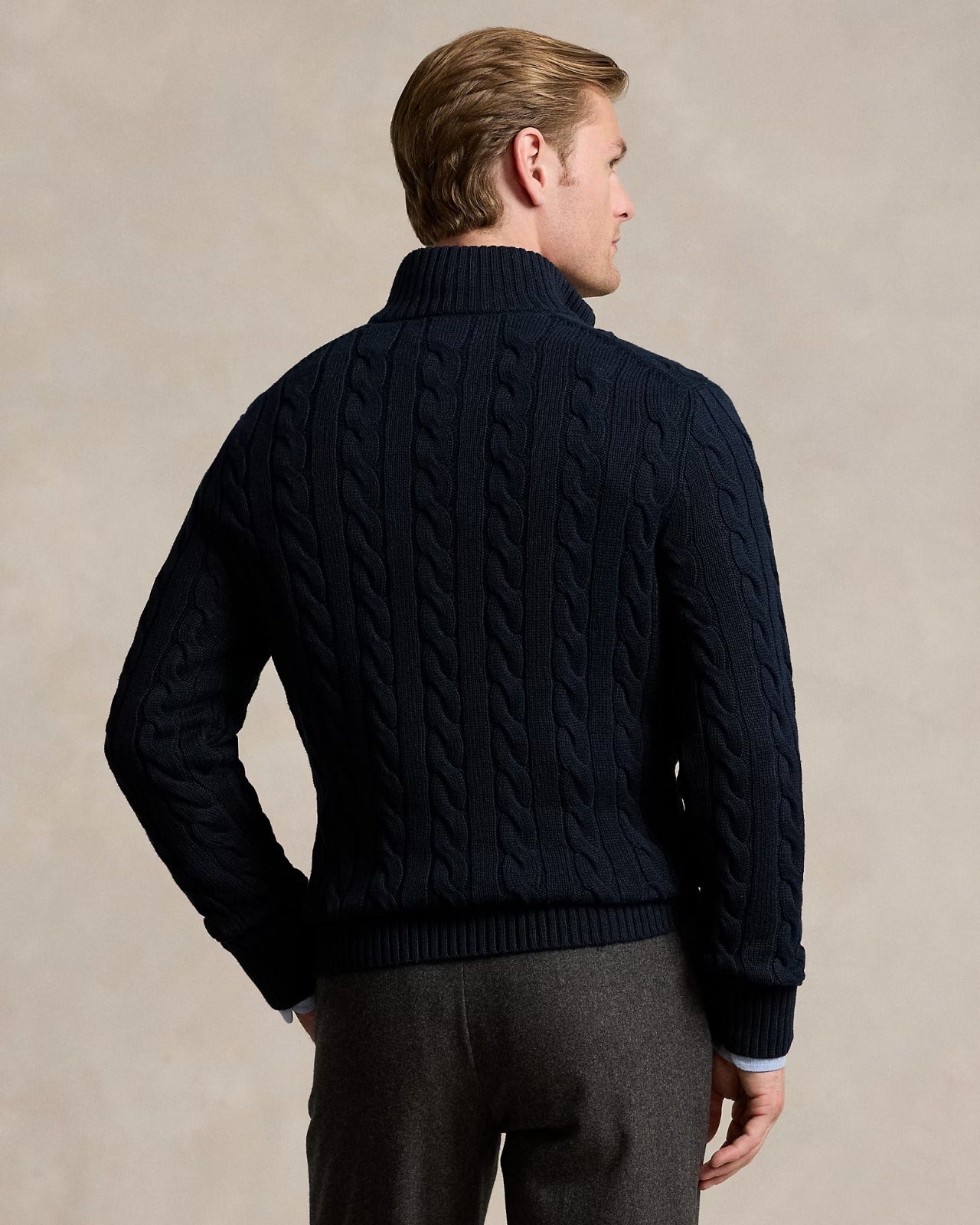 Back view of a male model wearing a cable-knit quarter-zip sweater in dark navy, showcasing its textured design.